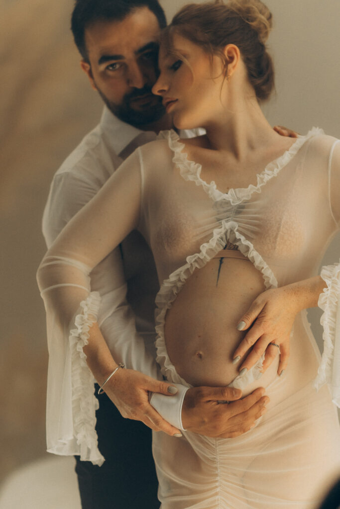 Soon-to-be parents smiling at each other, bathed in warm light during their Barcelona studio shoot.