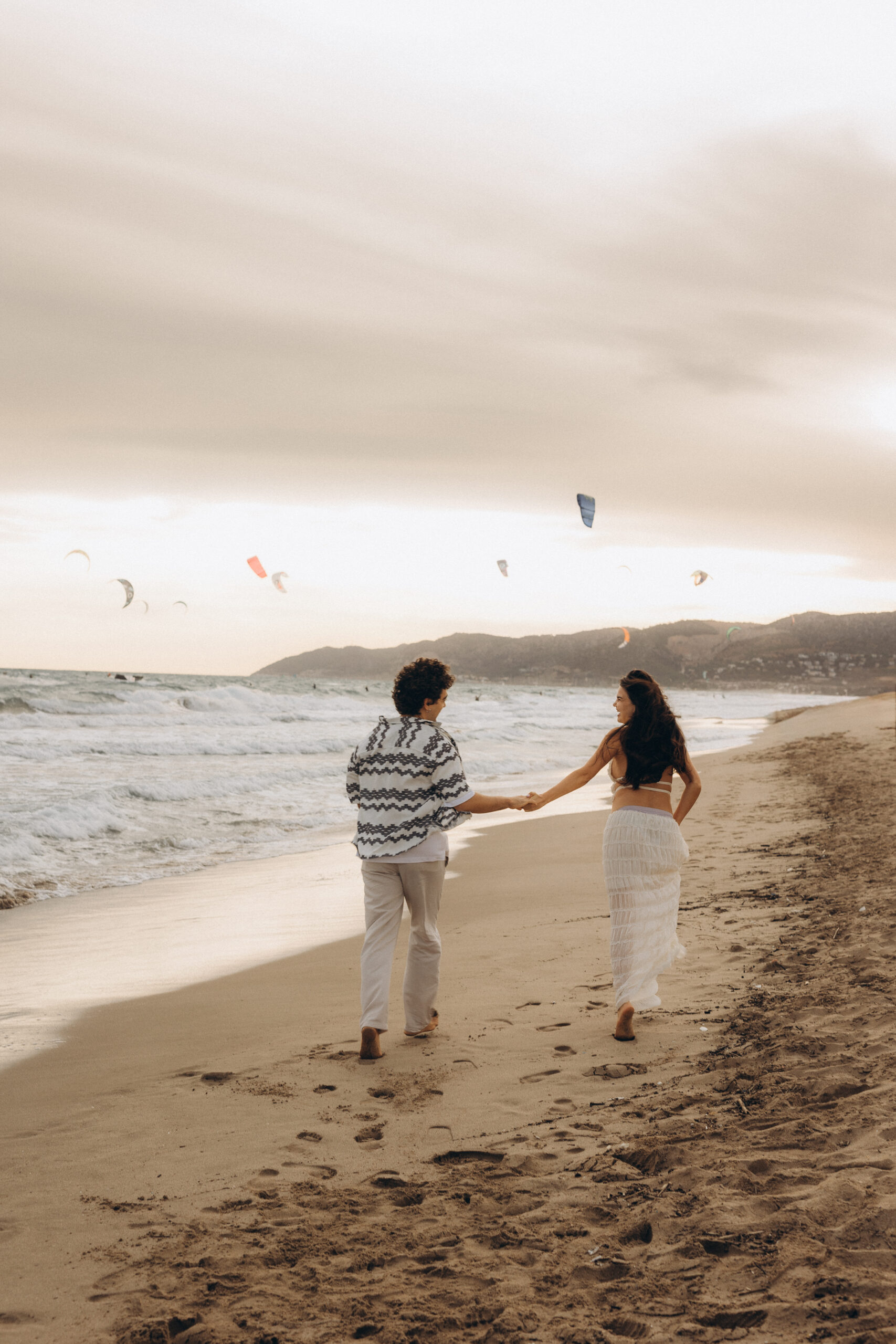 A couple is running along the sea cost in Barcelona during Sunset. beat poses for couple in the beach